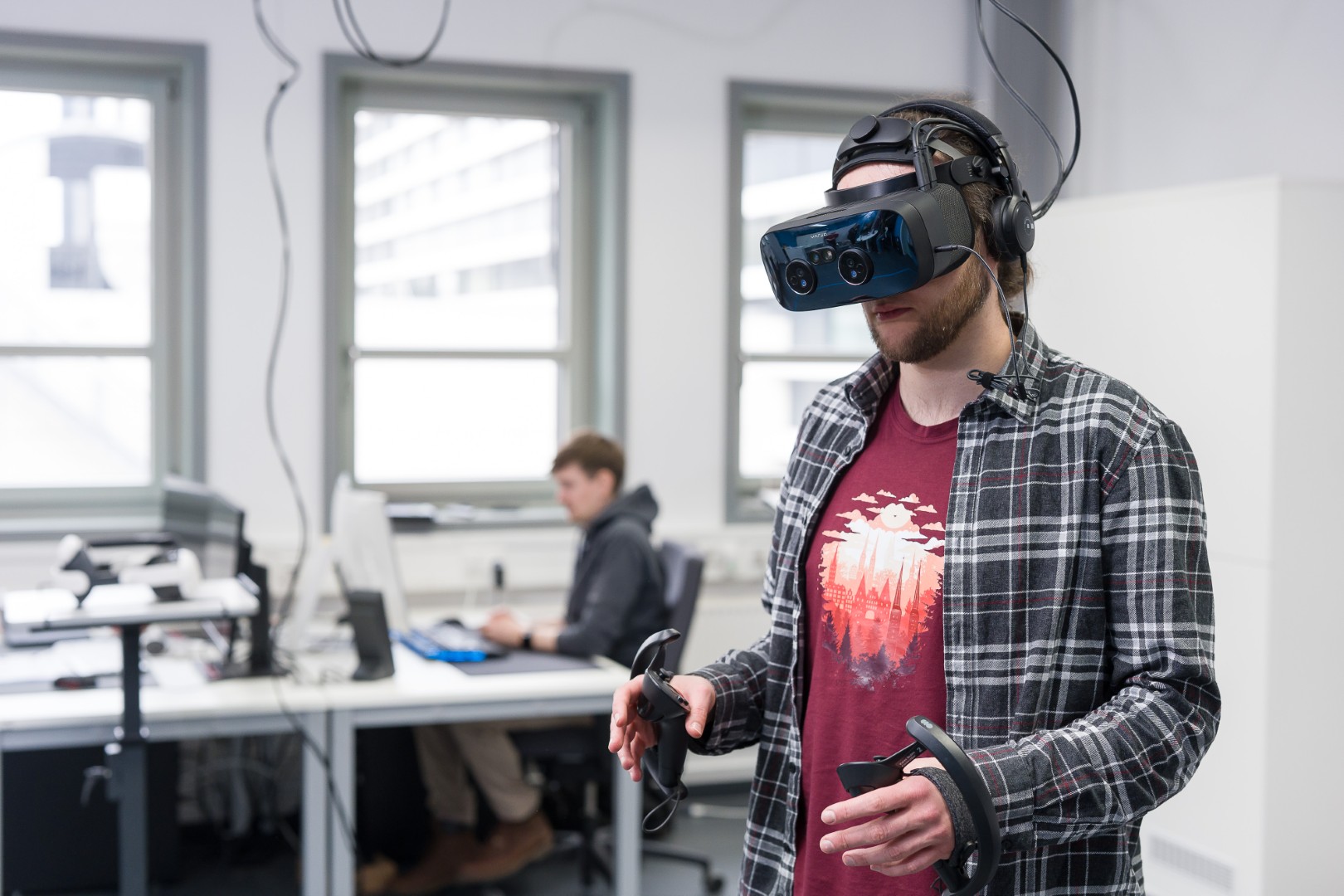 Die Person vorne hat eine VR Brille auf (Varjo XR3). Eine weitere Person sitzt hinten am PC.