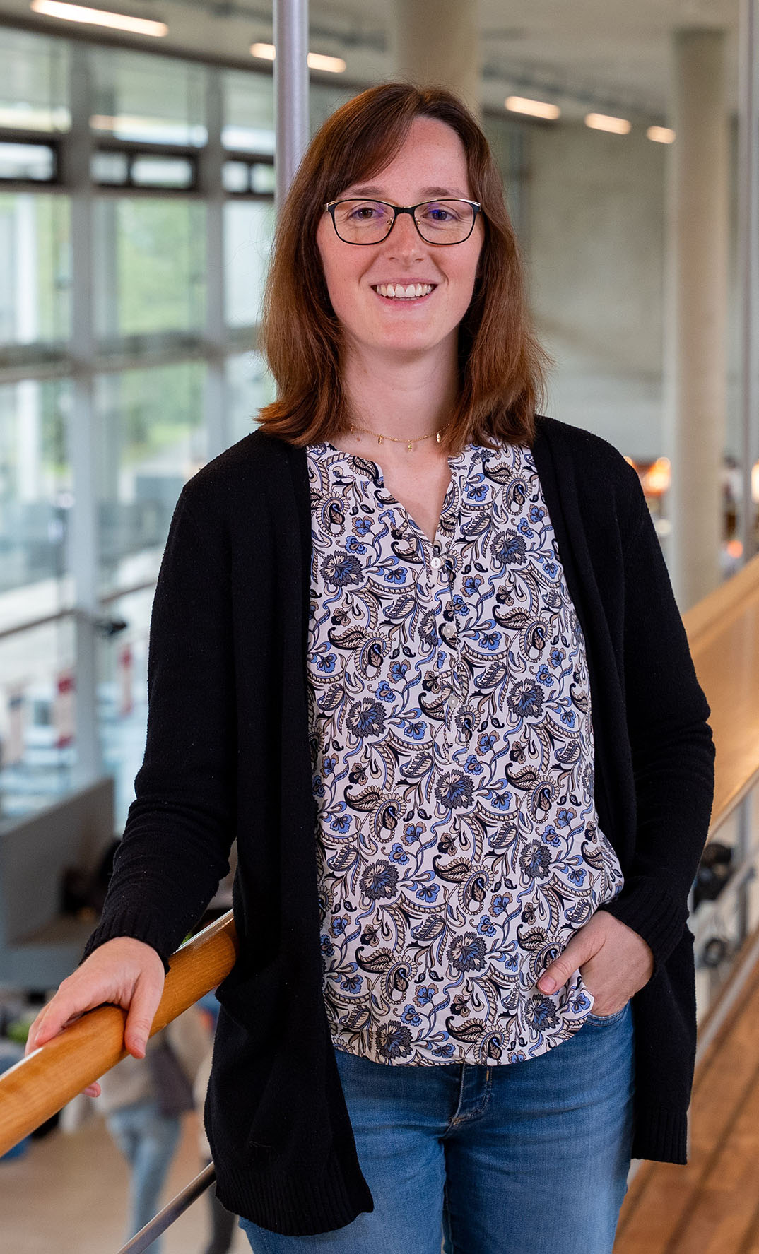 Frau steht lächelnd am Geländer im 1. Stock im Foyer der FH Westküste